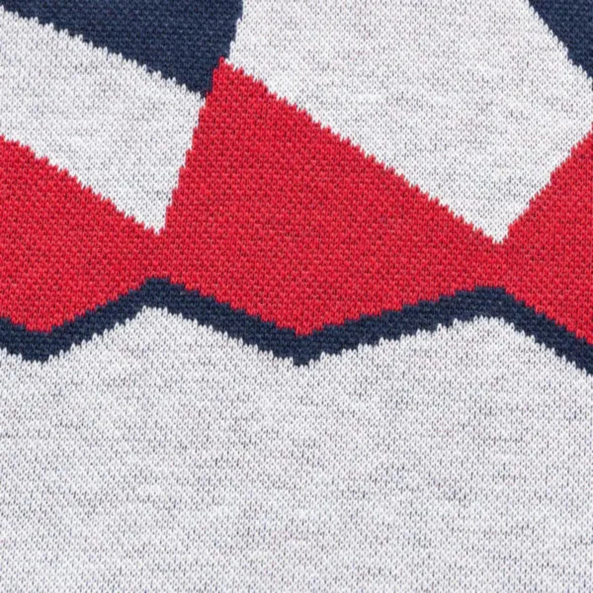 Close-up of a knitted fabric with a geometric pattern showing red and black zigzag shapes on white, reminiscent of the Limited Edition Blues Super Rugby 25/26 Retro Jersey by Classic Sportswear.
