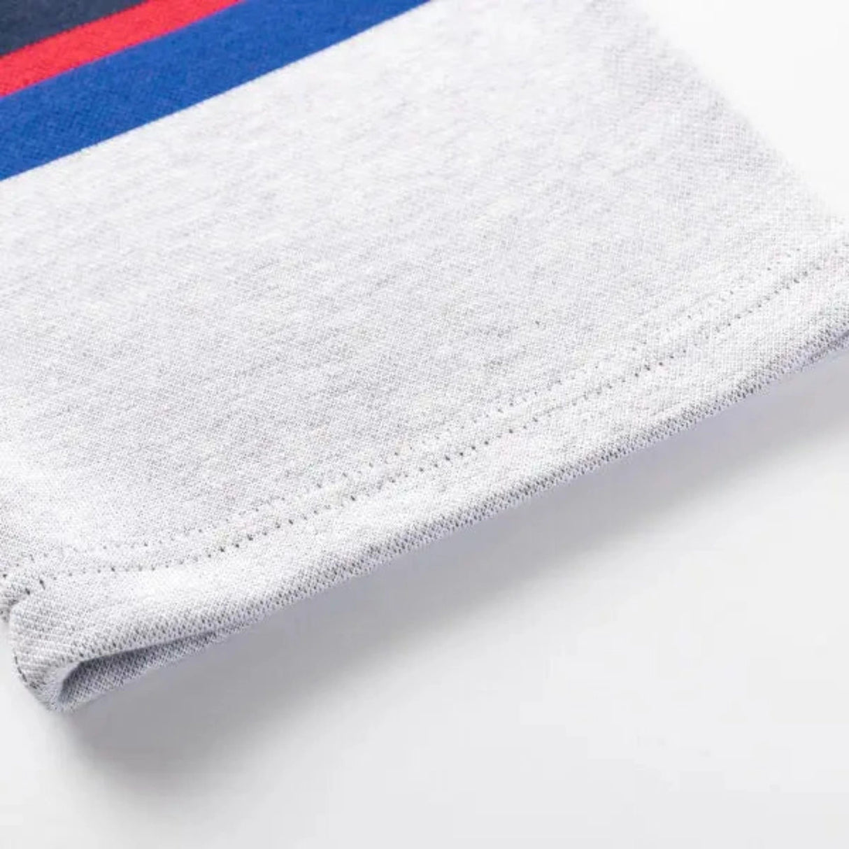 A close-up of the Limited Edition Blues Super Rugby 25/26 Retro Jersey by Classic Sportswear shows a gray fabric with red and blue stripes at the top edge, evoking a nostalgic jersey style.