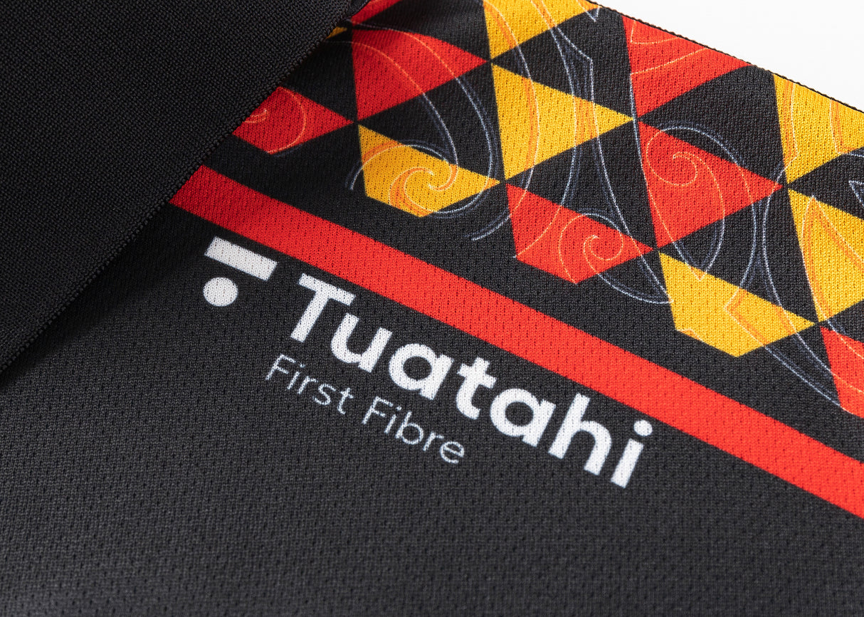 Close-up of black moisture-wicking fabric featuring colorful geometric patterns and the text "Tuataki First Fibre," alongside the Gallagher Chiefs Super Rugby logo, from the Gallagher Chiefs Super Rugby 25/26 Team Polo by Classic Sportswear.