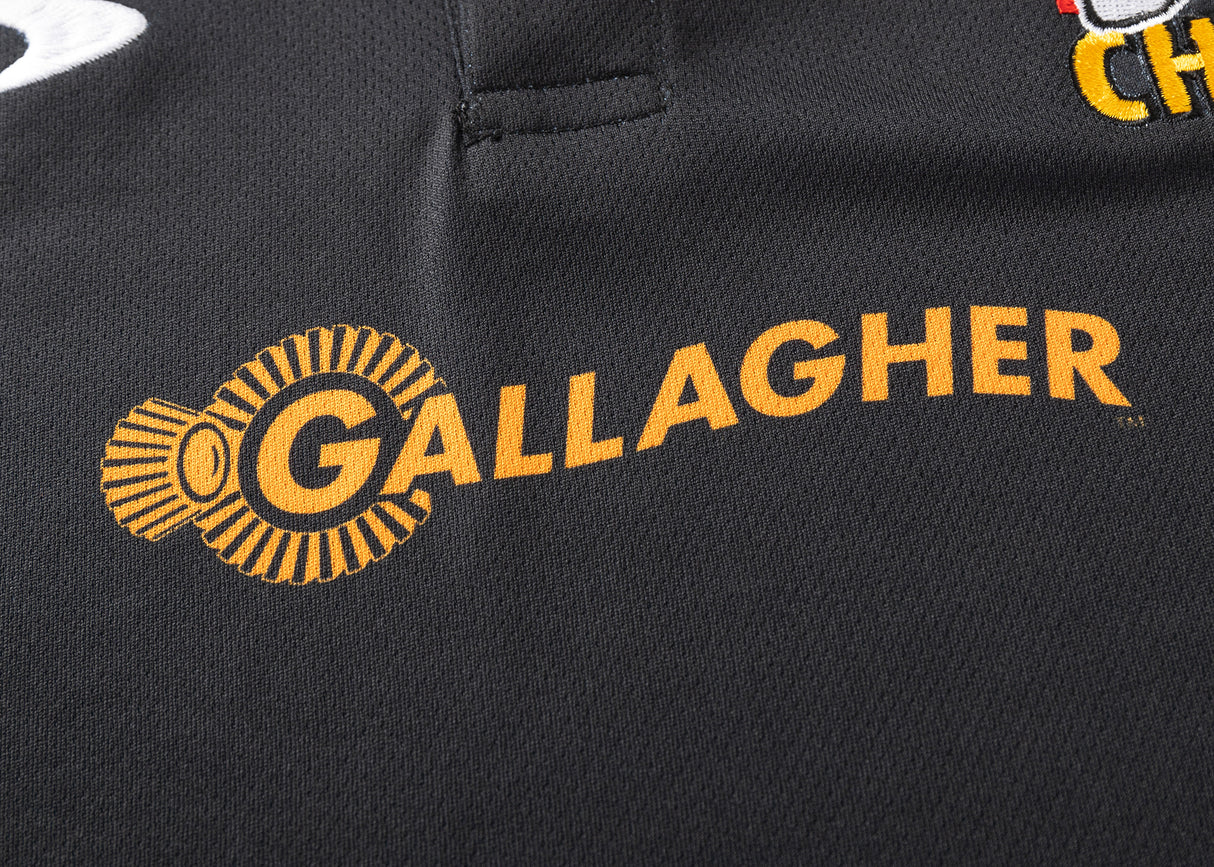 The Gallagher Chiefs Super Rugby 25/26 Team Polo by Classic Sportswear showcases a close-up of black, moisture-wicking fabric featuring "GALLAGHER" and the orange circular Chiefs logo, embodying the Chiefs Super Rugby spirit.