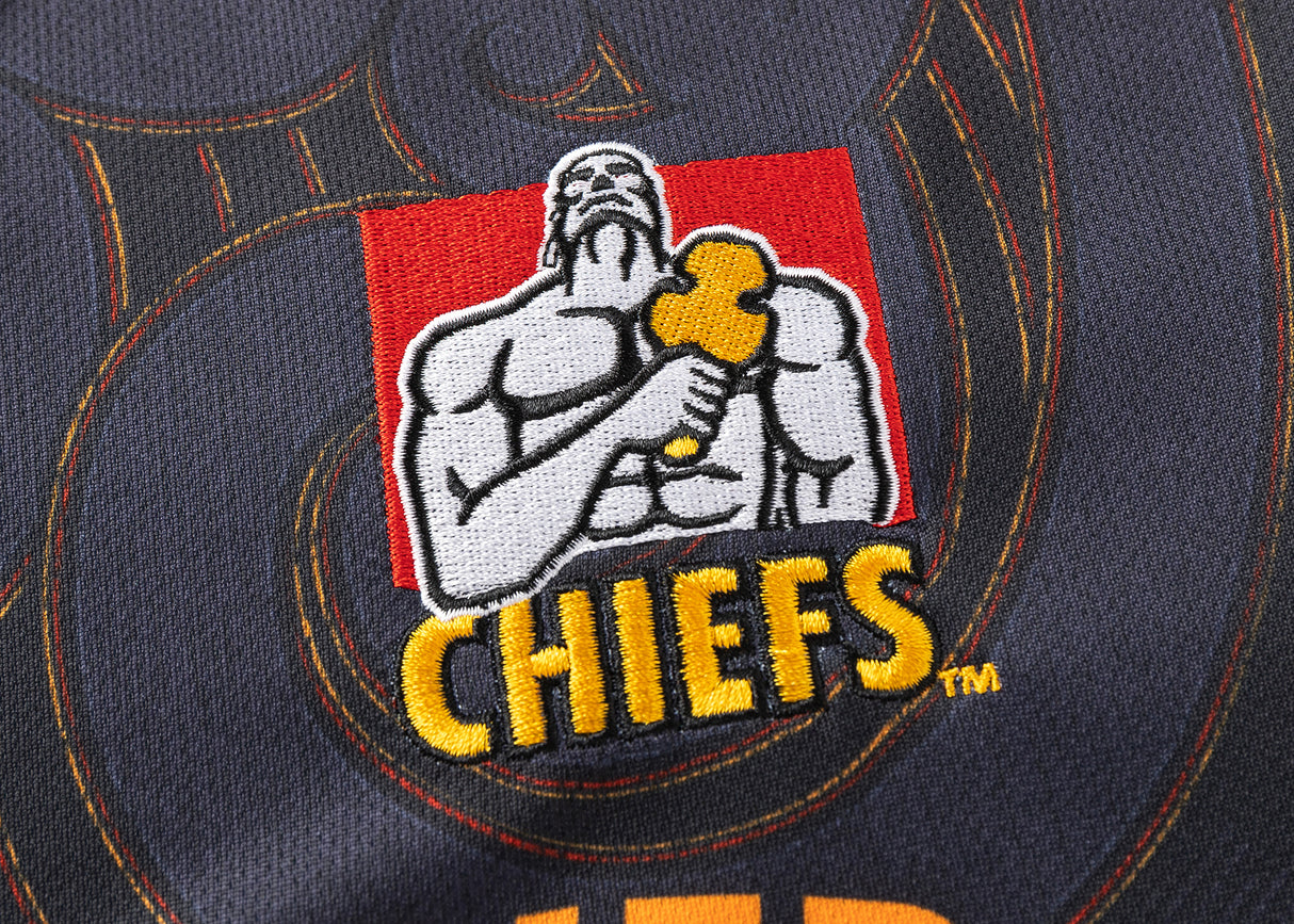Fabric adorned with a muscular figure holding a hammer and "CHIEFS" in bold yellow letters, this Gallagher Chiefs Super Rugby Replica Home Jersey 25/26 by Classic Sportswear embodies team spirit and pride.