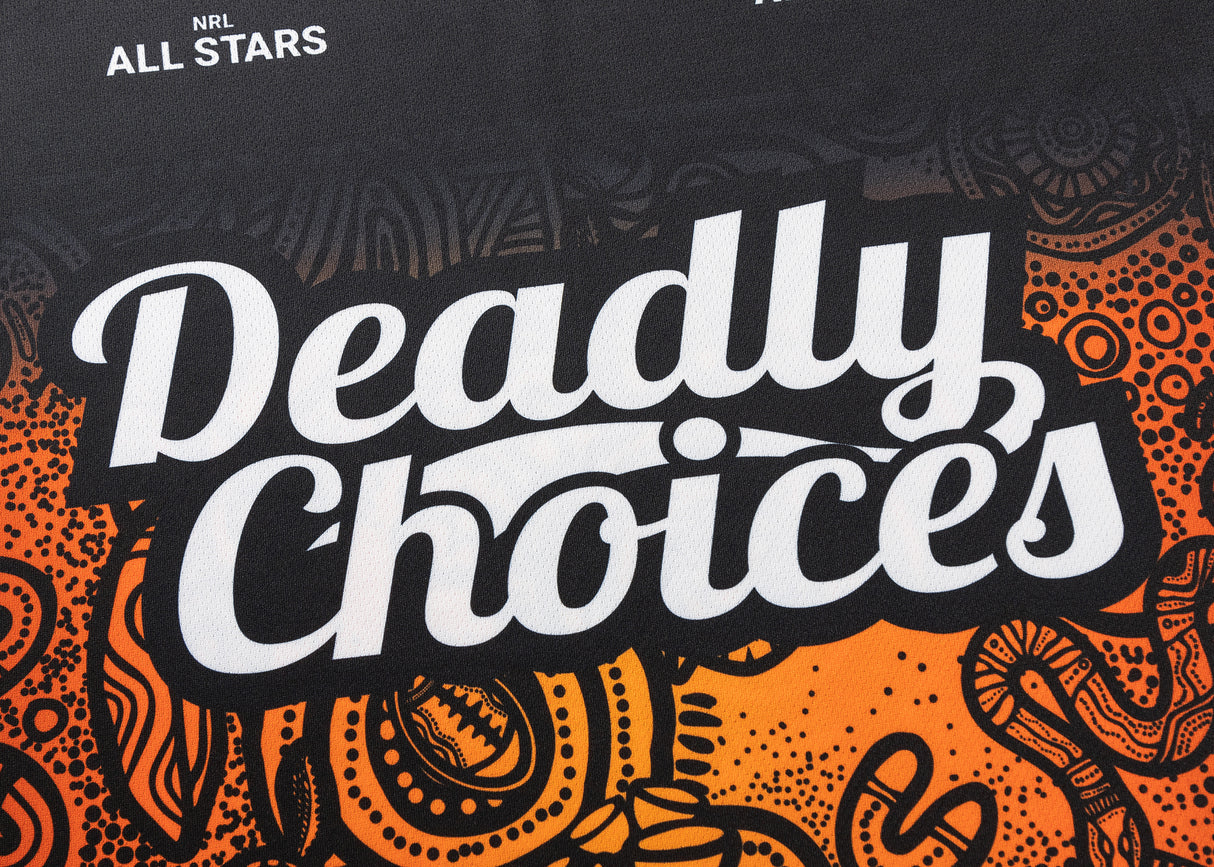 The image displays "Deadly Choices" in white on a black and orange backdrop with intricate patterns, along with "NRL Indigenous All Stars," capturing the vibrant spirit of the Classic Sportswear NRL Indigenous All Stars 25/26 Pro Training Singlet.