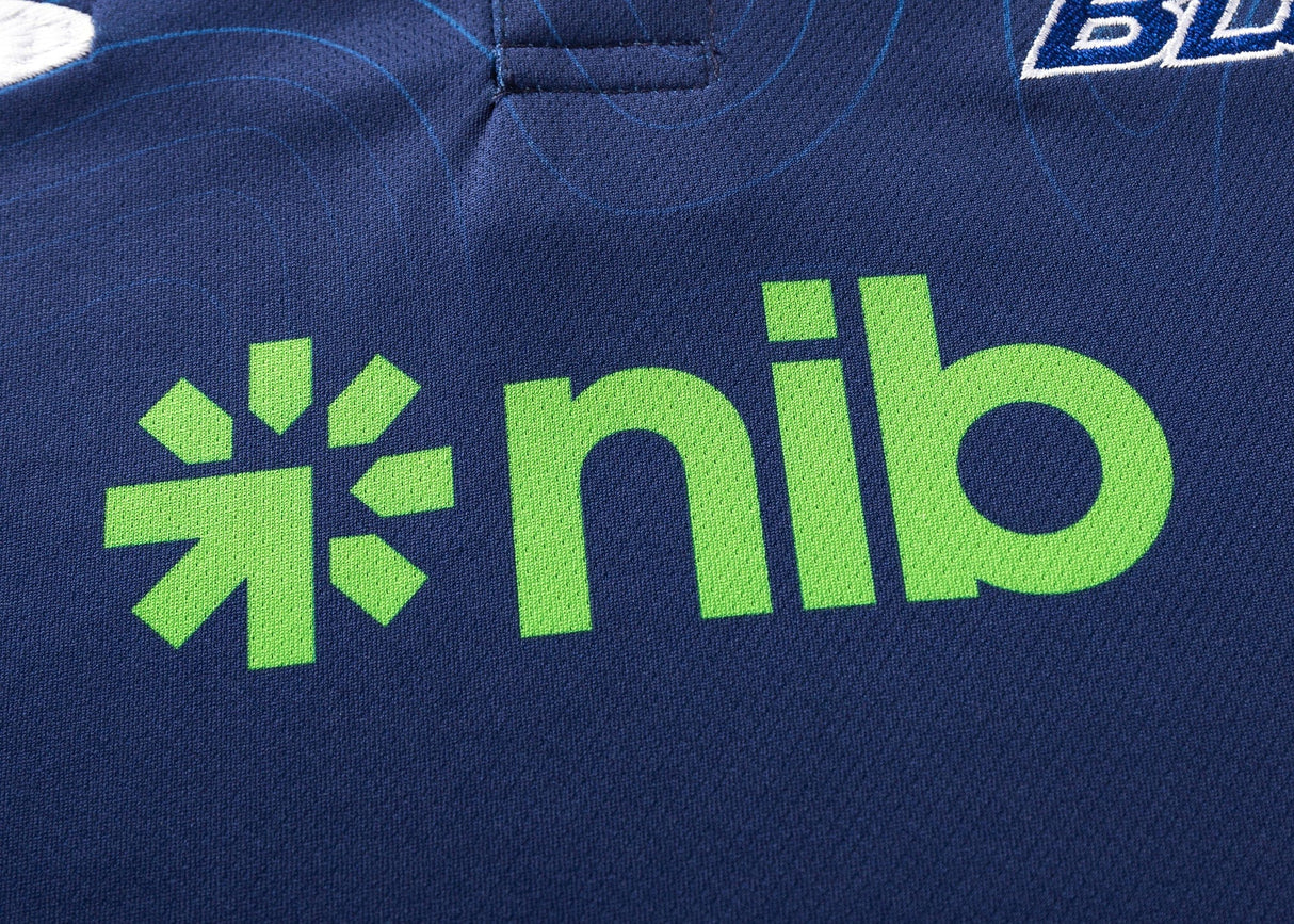 Close-up of a dark blue polo with the green "nib" logo. The Blues Super Rugby 25/26 Team Polo by Classic Sportswear exudes timeless sportswear charm, blending heritage and performance in every stitch.