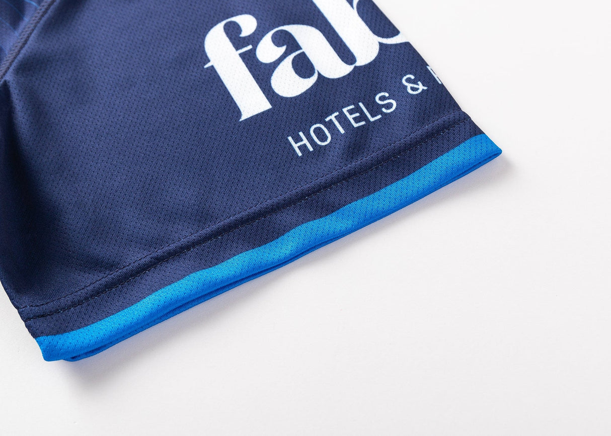 Close-up of a dark blue garment with a lighter blue edge, featuring partially visible white text showing "Hotels." This piece could easily be part of the Blues Super Rugby 25/26 Team Polo by Classic Sportswear collection.