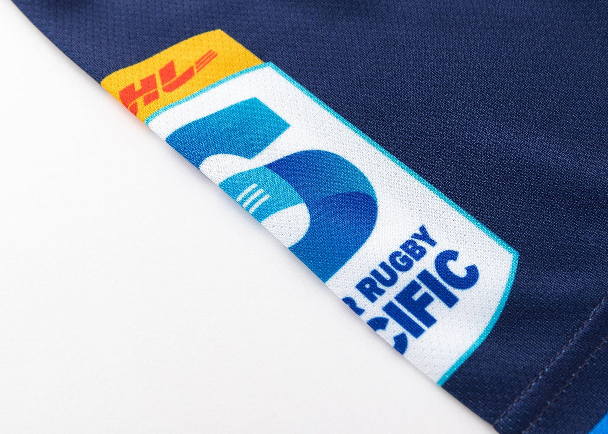 Close-up of the Blues Super Rugby 25/26 Team Polo by Classic Sportswear, showing part of the team logo with "5" and "Rugby Pacific" on navy blue fabric.