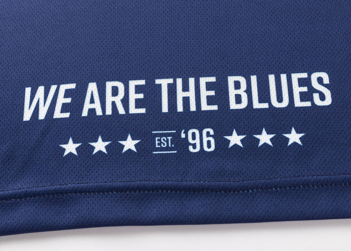 The Blues Super Rugby 25/26 Team Polo by Classic Sportswear features navy blue fabric with "WE ARE THE BLUES" in white text above "EST. '96," flanked by stars, celebrating the heritage of Blues Super Rugby.
