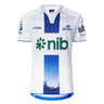 The Blues Super Rugby 25/26 Replica Away Jersey by Classic Sportswear showcases a white and blue design with the "nib" logo in green and the Blues emblem on the chest. A cityscape adorns the bottom, while sponsor logos decorate the sleeves, appealing to true Blues fans.