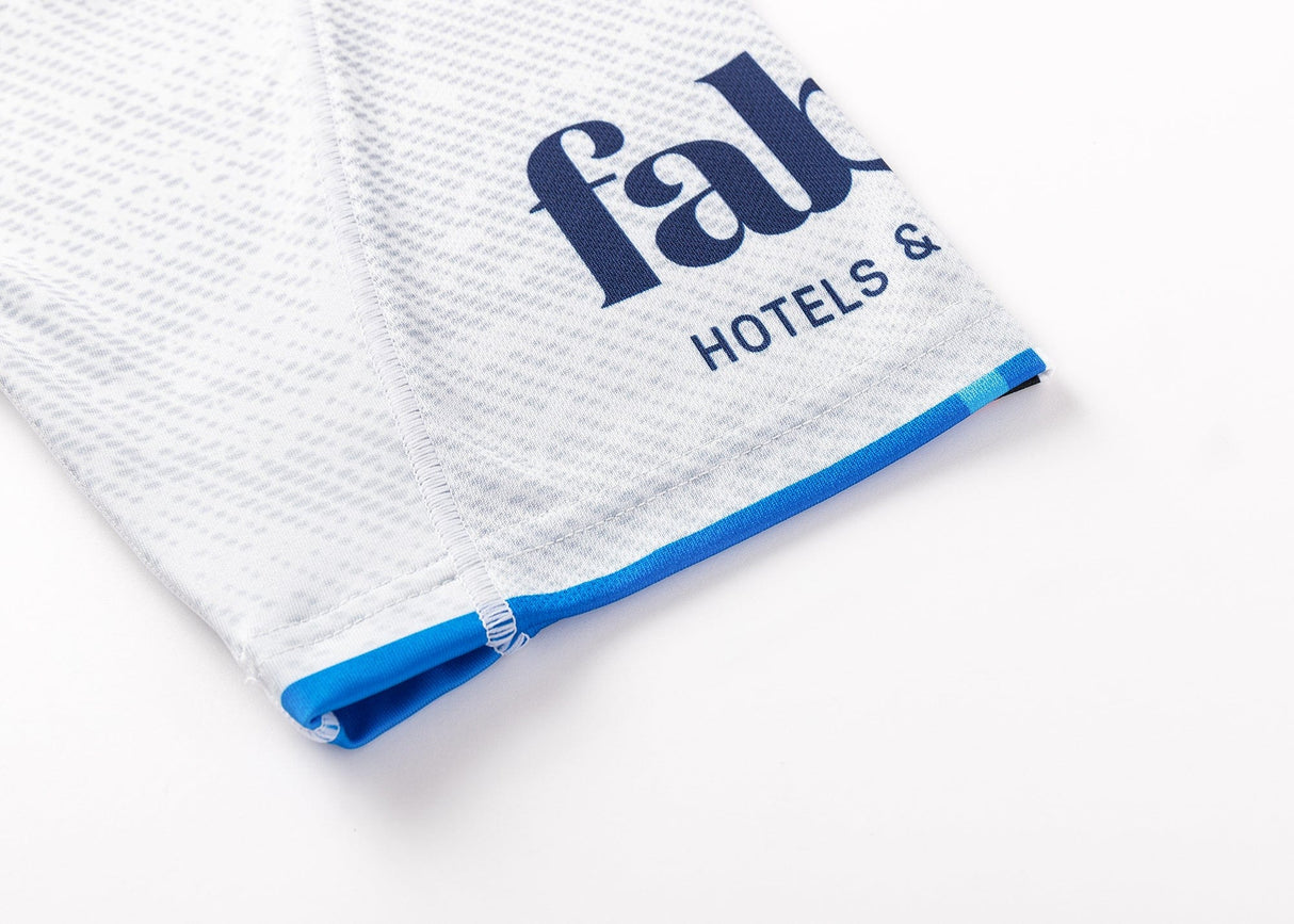 Close-up of white textured fabric with blue stitching resembling classic sportswear, featuring partial blue text "fab" and "HOTELS &", reminiscent of the sleek design from the Blues Super Rugby 25/26 Replica Away Jersey by Classic Sportswear.