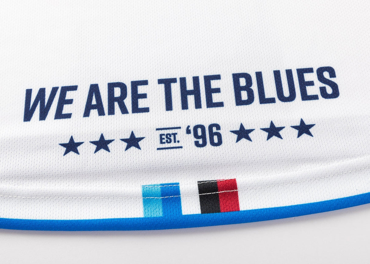 Close-up of the Blues Super Rugby 25/26 Replica Away Jersey by Classic Sportswear in white, featuring "WE ARE THE BLUES" and "EST. '96" in blue, with six stars. Stripes in blue, black, and red adorn the bottom, capturing the iconic Blues rugby spirit with a classic touch.