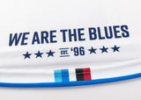 Close-up of the Blues Super Rugby 25/26 Replica Away Jersey by Classic Sportswear in white, featuring "WE ARE THE BLUES" and "EST. '96" in blue, with six stars. Stripes in blue, black, and red adorn the bottom, capturing the iconic Blues rugby spirit with a classic touch.