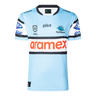 The Sharks NRL 25/26 Replica Home Jersey by Classic Sportswear features a light blue design with black and white striped sleeves, adorned with Pilot, Aramex, and Cronulla Sutherland Sharks logos. A must-have for any Sharks fan.