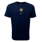 The Racing 92 Evergreen Tee 1 by Nike is a navy blue tee designed from premium cotton jersey, adorned with a small golden shield emblem and a gold Nike swoosh logo on the chest.