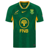 Introducing the Springboks 26/27 Greatest Rivalry Replica Home Jersey by Nike. This authentic replica rugby jersey features iconic green with yellow accents, sponsor logos, the Springboks emblem, and a subtle printed text pattern. Complete with the South African flag on the sleeve, it’s the perfect choice for dedicated fans of Nike and South Africa rugby.