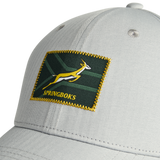 Close-up of the Nike Springboks 26/27 RGR Legacy 91 Club Cap in light gray, showcasing a rectangular green patch with yellow trim, an antelope design, and “SPRINGBOKS” embroidered at the front—a must-have accessory for any rugby fan.