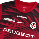Stade Toulousain Home Pre-Match SS Top by Nike in a red and black pattern, featuring short sleeves and the Airbus, Kumho, Peugeot, and team crest logos on the chest.