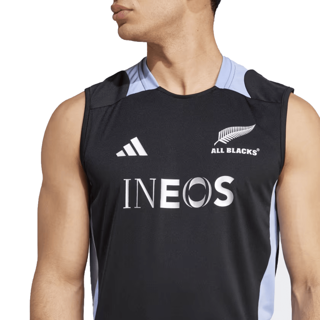A person wearing an Adidas All Blacks 24/25 Performance Singlet, which is black and showcases the iconic All Blacks logo along with the word "INEOS" on the front.