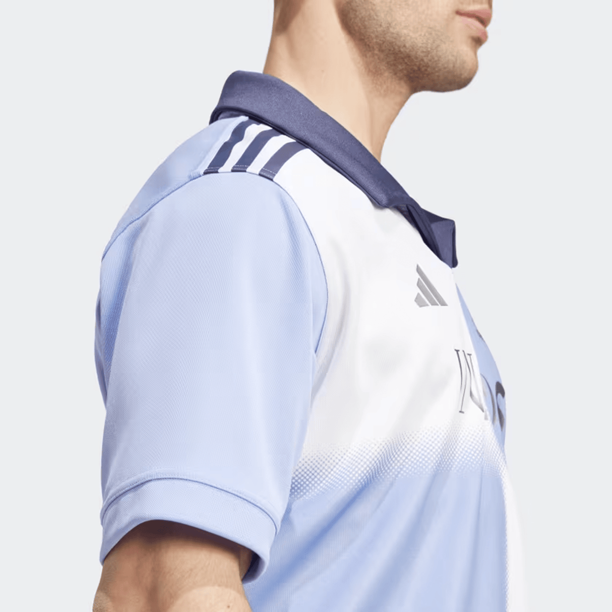 A person in the All Blacks 24/25 Training Jersey by adidas, featuring light blue and white with dark blue collar and shoulder stripes, captures the essence of an iconic All Blacks jersey style.