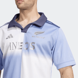 Someone wears the adidas All Blacks 24/25 Training Jersey in a light blue and white gradient with a striking collar, featuring the silver fern and logos of adidas and Ineos on the front.