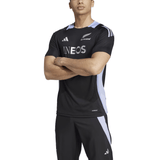 A person wearing an All Blacks 24/25 Performance T-Shirt by adidas and black sports pants stands with arms crossed, showcasing AEROREADY technology for optimal comfort.