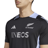 A person wearing the All Blacks 24/25 Performance T-Shirt by Adidas, adorned with the "All Blacks" silver fern emblem and INEOS sponsor logo, showcases cutting-edge AEROREADY technology for maximum comfort.