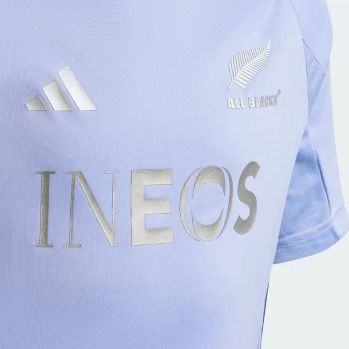 Close-up of a light blue All Blacks 24/25 Performance T-Shirt by adidas, featuring AEROREADY technology. The shirt prominently displays the All Blacks and adidas logos, with "INEOS" elegantly rendered in silver lettering.