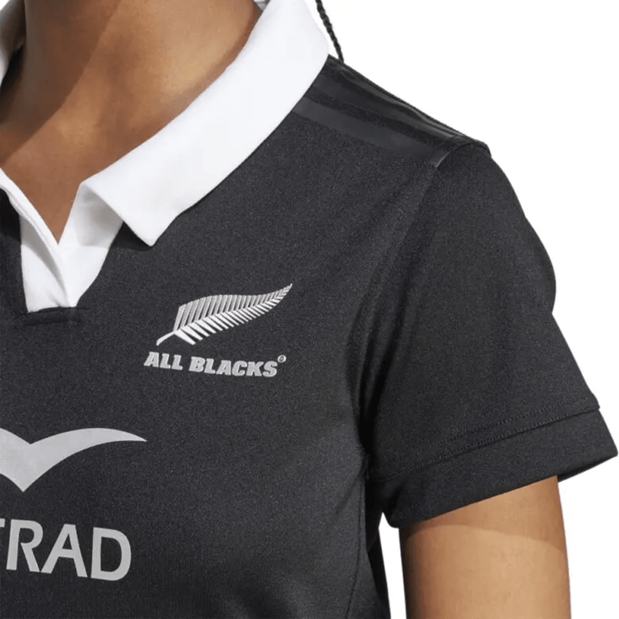 A close-up of a person wearing an adidas Women's All Blacks 24/25 Home Supporters Jersey, proudly displaying the "ALL BLACKS" name and a silver fern emblem, with AEROREADY technology for ultimate comfort and performance.