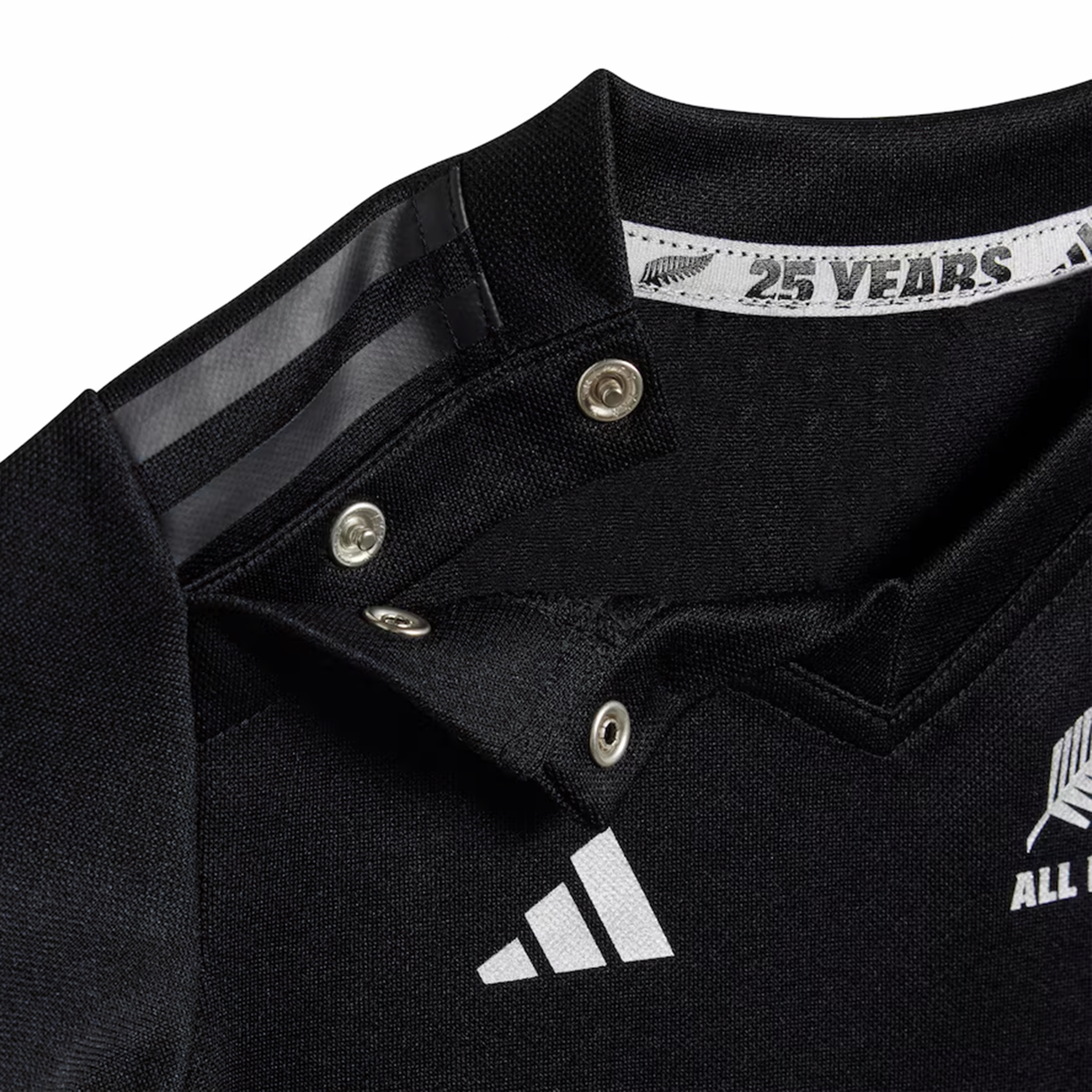Close-up of an adidas Infant All Blacks 24/25 Home Kit sports jersey collar with snap buttons, featuring white logos and "25 YEARS" text, crafted with AEROREADY Technology.