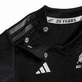 Close-up of an adidas Infant All Blacks 24/25 Home Kit sports jersey collar with snap buttons, featuring white logos and "25 YEARS" text, crafted with AEROREADY Technology.