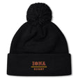 The Iona College Pom Pom Beanie by EMB Canterbury is a black fleece-lined hat featuring a pom-pom and "IONA RUGBY" embroidered in gold and red on the front cuff.