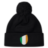 The EMB Canterbury Ireland Shield Pom Pom Beanie features a stylish shield emblem with green, white, and orange vertical stripes, reminiscent of the Ireland flag.