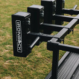 A close-up of the IronBack Gorilla 8 Man Scrum Machine, a black rugby scrum trainer with padded sections, shown on grass outdoors.