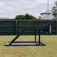 An IronBack Ironback Gorilla 8 Man Scrum Machine in black metal stands on a grassy lawn, with a green wooden fence and houses in the background.