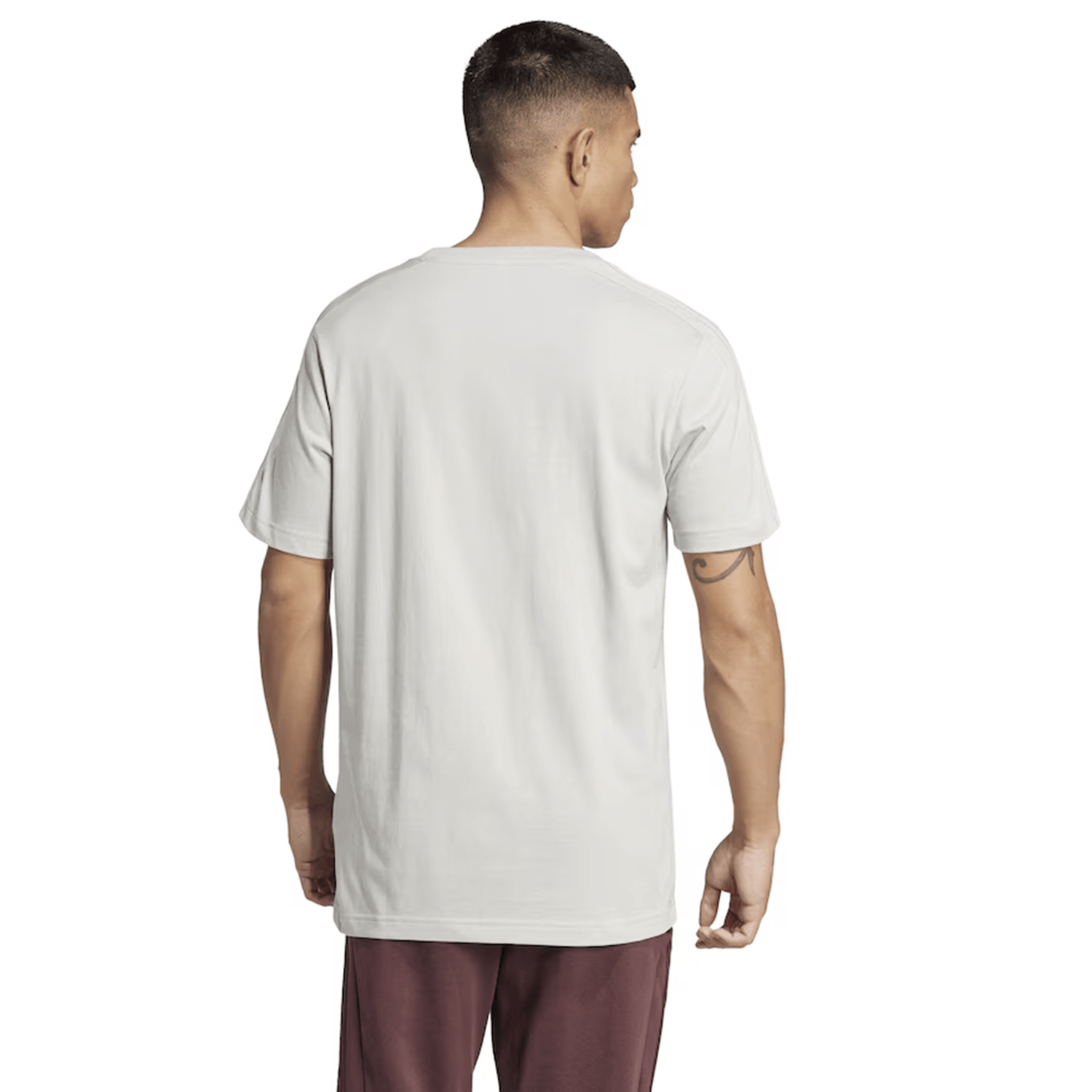 A person with short hair is standing with their back to the camera, wearing a plain light-colored All Blacks 24/25 Fan Tee by adidas and maroon pants.