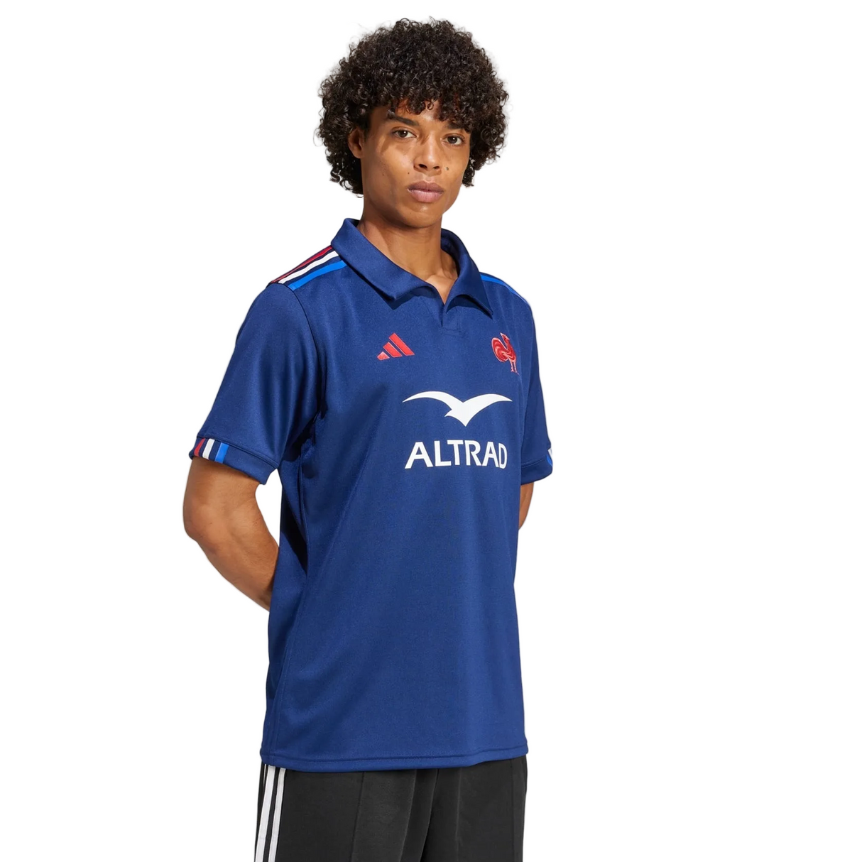 A person stands with hands behind their back, wearing the adidas France FFR 25/26 Replica Home Jersey—a blue short-sleeve collared shirt with red and white logos and "ALTRAD" on the front.