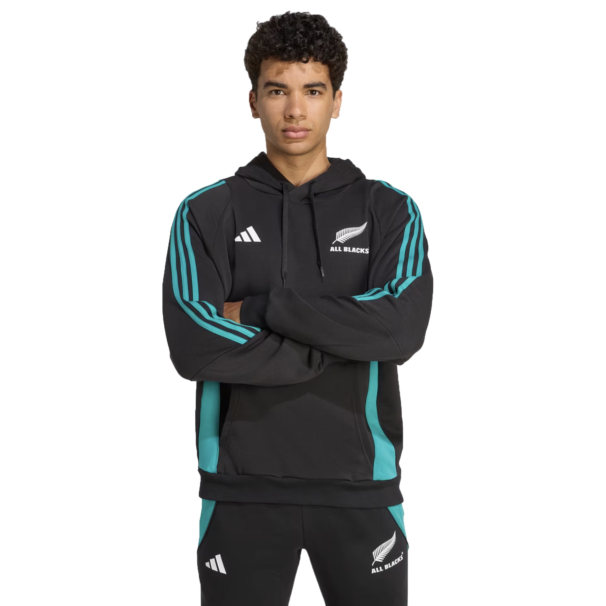 A person stands with arms crossed, wearing the adidas All Blacks 25/26 Training Hoodie and matching pants with adidas logos, against a plain white background.