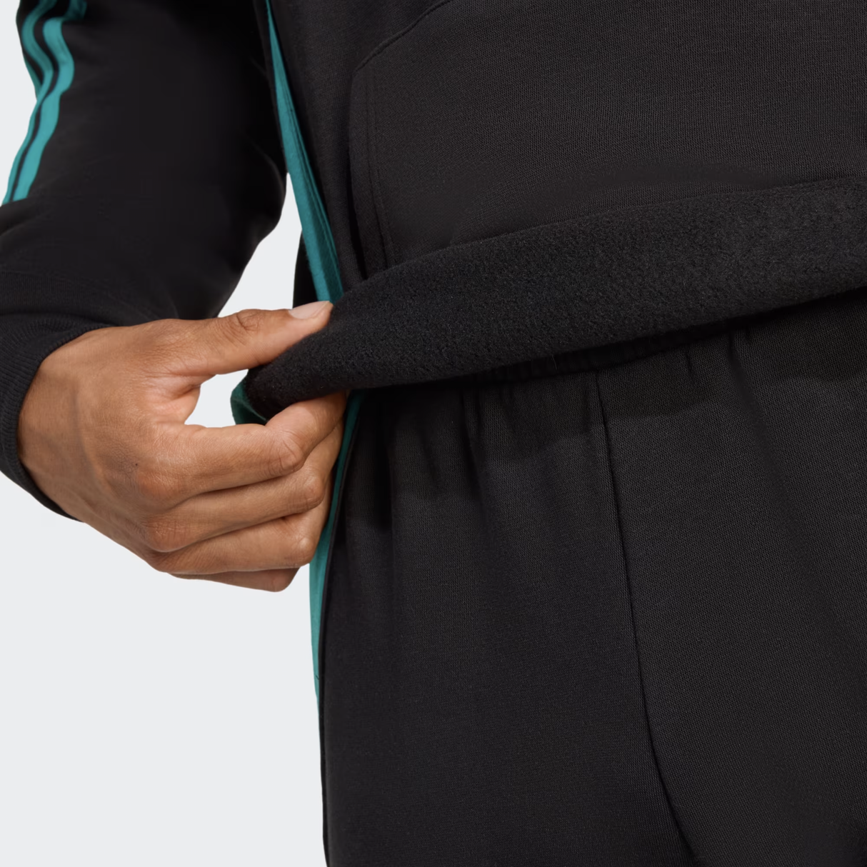 Someone lifts the hem of an adidas All Blacks 25/26 Training Hoodie, revealing its soft inner lining.