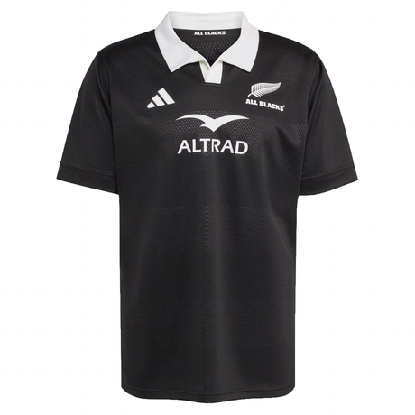 The All Blacks 25/26 Replica Home Jersey by adidas is a black short-sleeve jersey made from recycled polyester, featuring a white collar, adidas logo, silver fern All Blacks logo, and "ALTRAD" sponsor text on the chest.