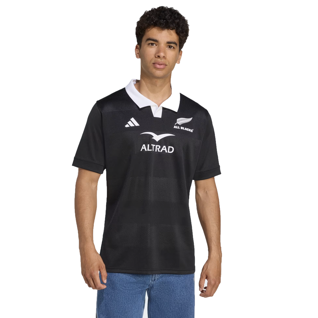 A man stands against a white background wearing the All Blacks 25/26 Replica Home Jersey by adidas, featuring a black design with a white collar and made from recycled polyester.