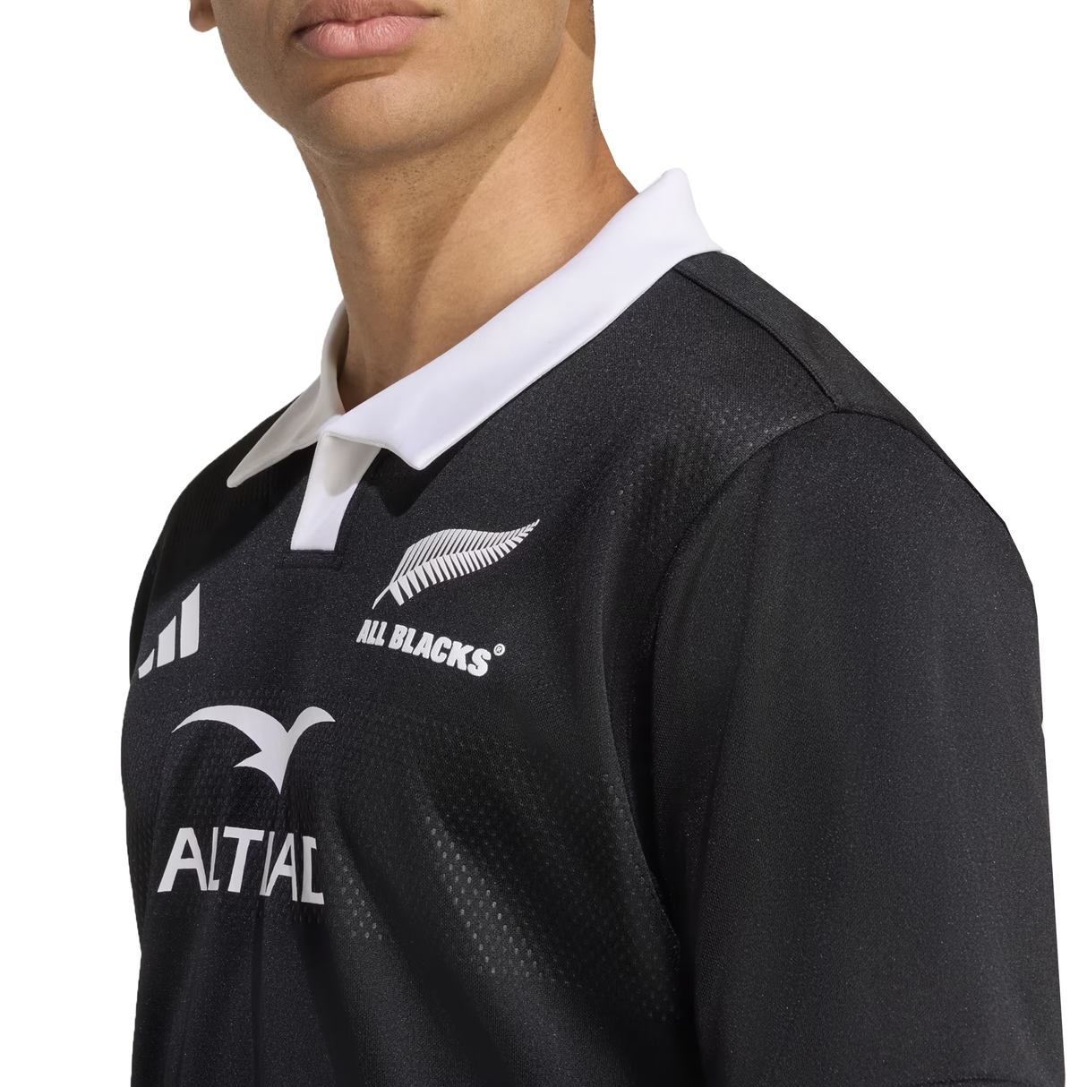 Someone wears the adidas All Blacks 25/26 Replica Home Jersey, featuring a white collar, team logos on the chest, and made from recycled polyester.