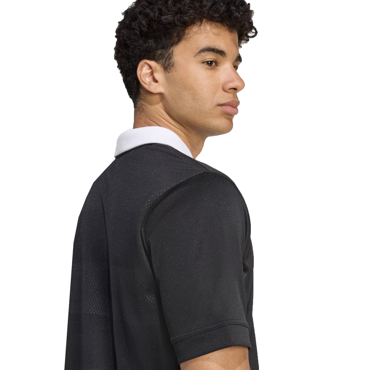 A person with short curly hair wears the adidas All Blacks 25/26 Replica Home Jersey, featuring a white collar, and looks over their shoulder against a plain white background.