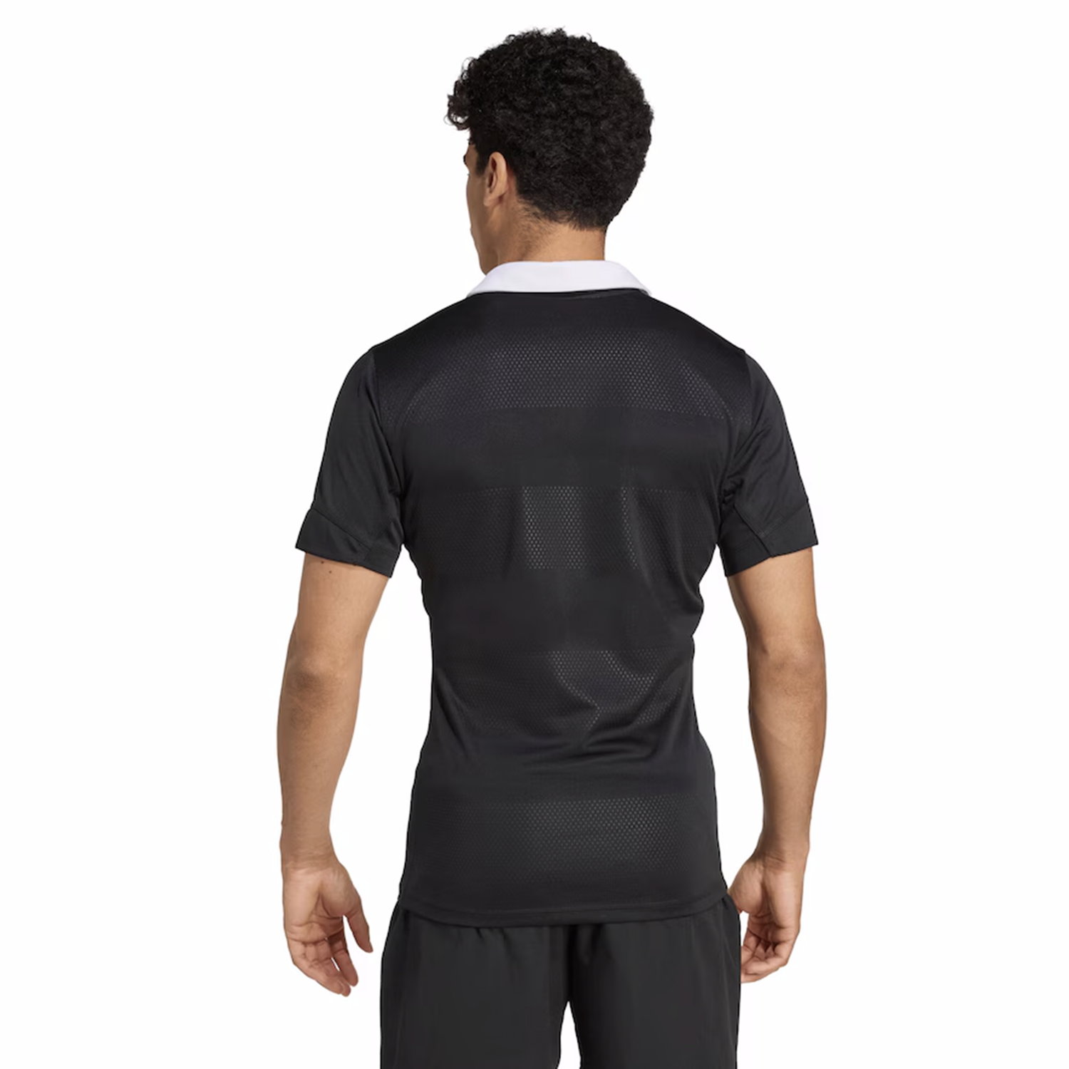 A man stands facing away, wearing the adidas All Blacks 25/26 Performance Home Jersey with a white collar and matching black shorts.