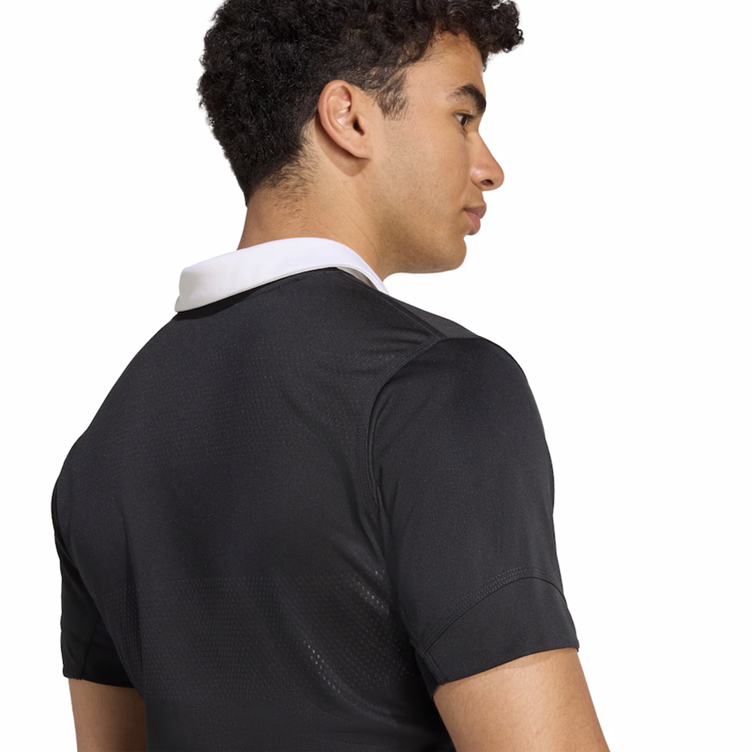 A man with short curly hair is seen from behind, wearing the adidas All Blacks 25/26 Performance Home Jersey—a black collared shirt with a distinctive white collar.