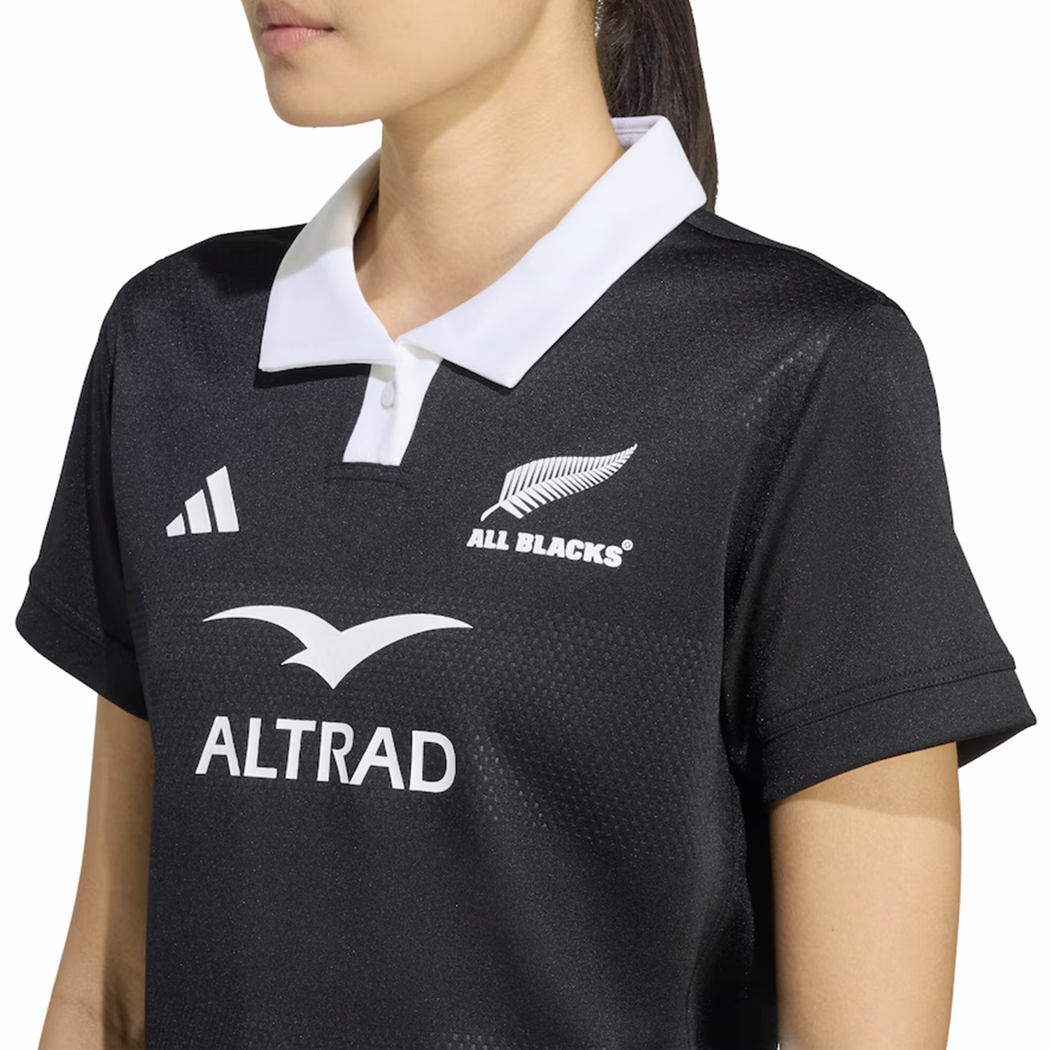 A woman wears the adidas Women's All Blacks 25/26 Replica Home Jersey, black with a white collar, featuring adidas logos and the iconic silver fern.