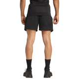 A person is standing facing away from the camera, wearing a black shirt, adidas All Blacks 25/26 Replica Home Shorts, black socks, and black shoes.