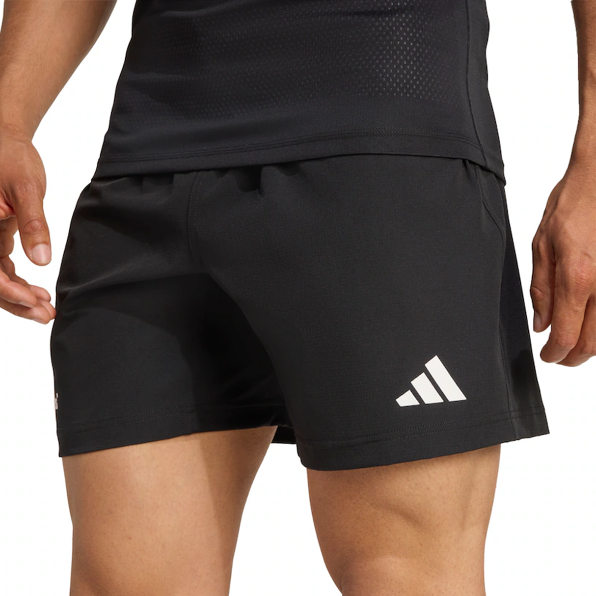 A person wearing black adidas All Blacks 25/26 Replica Home Shorts with a white adidas logo on the left leg, paired with a black athletic top.