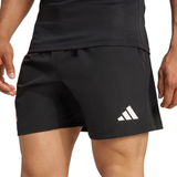 A person wearing black adidas All Blacks 25/26 Replica Home Shorts with a white adidas logo on the left leg, paired with a black athletic top.