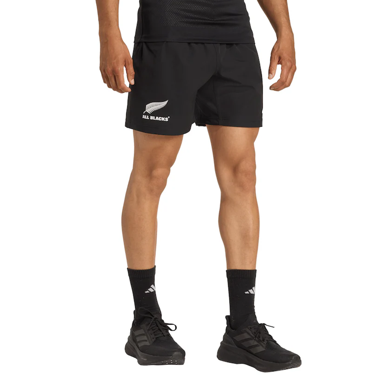 A person wearing adidas All Blacks 25/26 Replica Home Shorts, black sneakers, black socks, and a black shirt, shown from waist to feet.