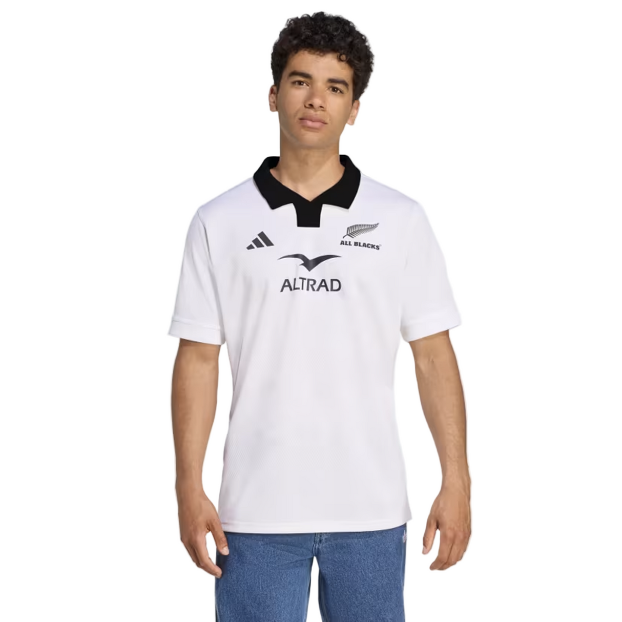 A person wears the adidas All Blacks 25/26 Replica Away Jersey, featuring a white design with black collar and adidas logos, styled as an away rugby jersey, paired with blue jeans, standing against a plain background.