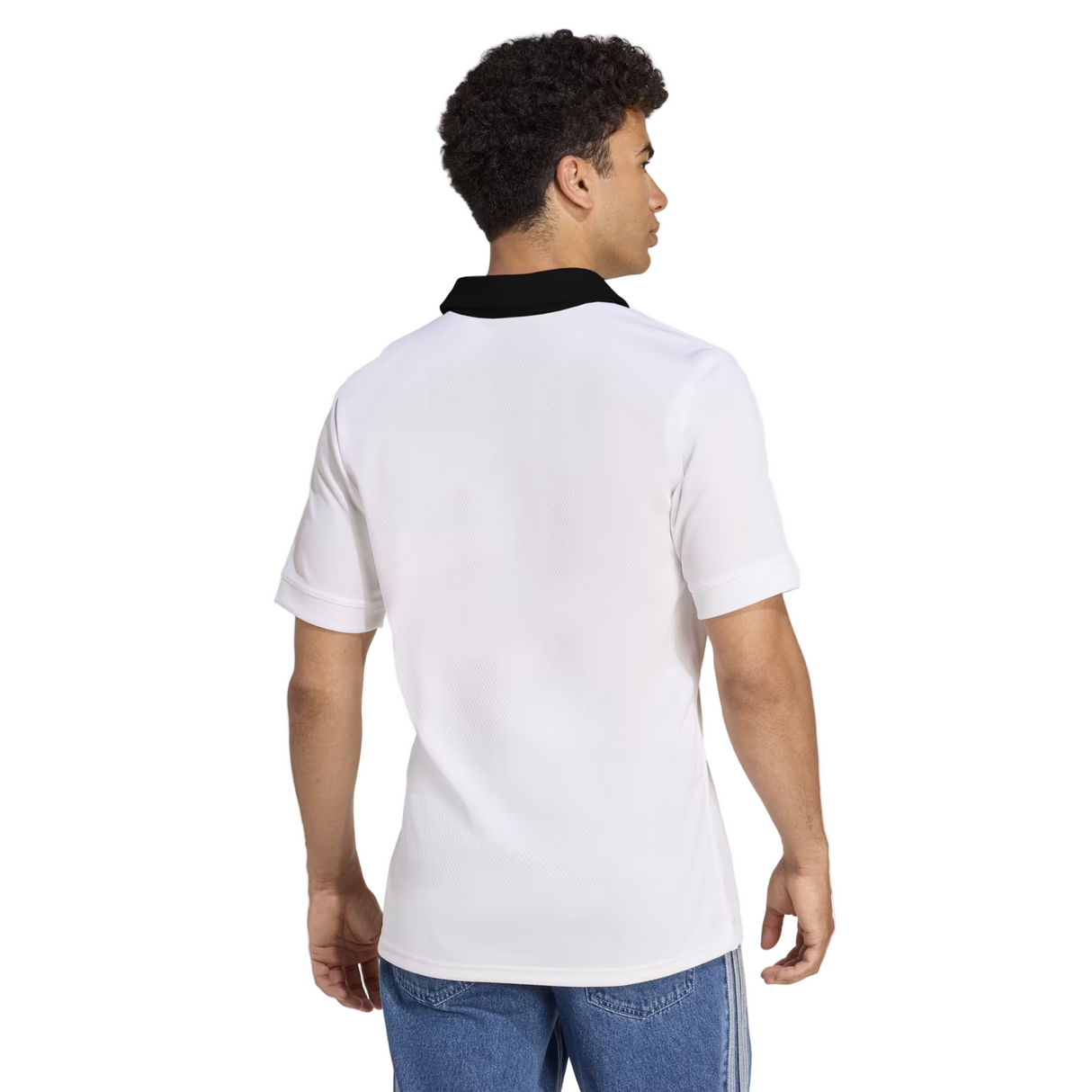 A person wearing the adidas All Blacks 25/26 Replica Away Jersey, a short-sleeve white rugby shirt with a black collar, paired with blue jeans, viewed from the back.