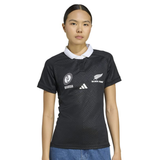 A woman wears the adidas Women's Black Ferns WRWC25 Replica Home Jersey, featuring a white collar and team logos, standing against a plain background with a neutral expression.